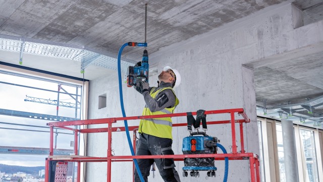 Ein Arbeiter steht auf einer Anhöhe und arbeitet mit einem Trockenbau-Werkzeug und bearbeitet eine Decke.
