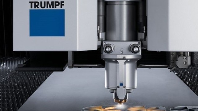 Eine Laser-Schneidemaschine, die Formen ausschneidet. Dahinter das Logo von Trumpf: ein blaues Rechteck mit dem Wort "Trumpf" darüber auf einer weißen Fläche.
